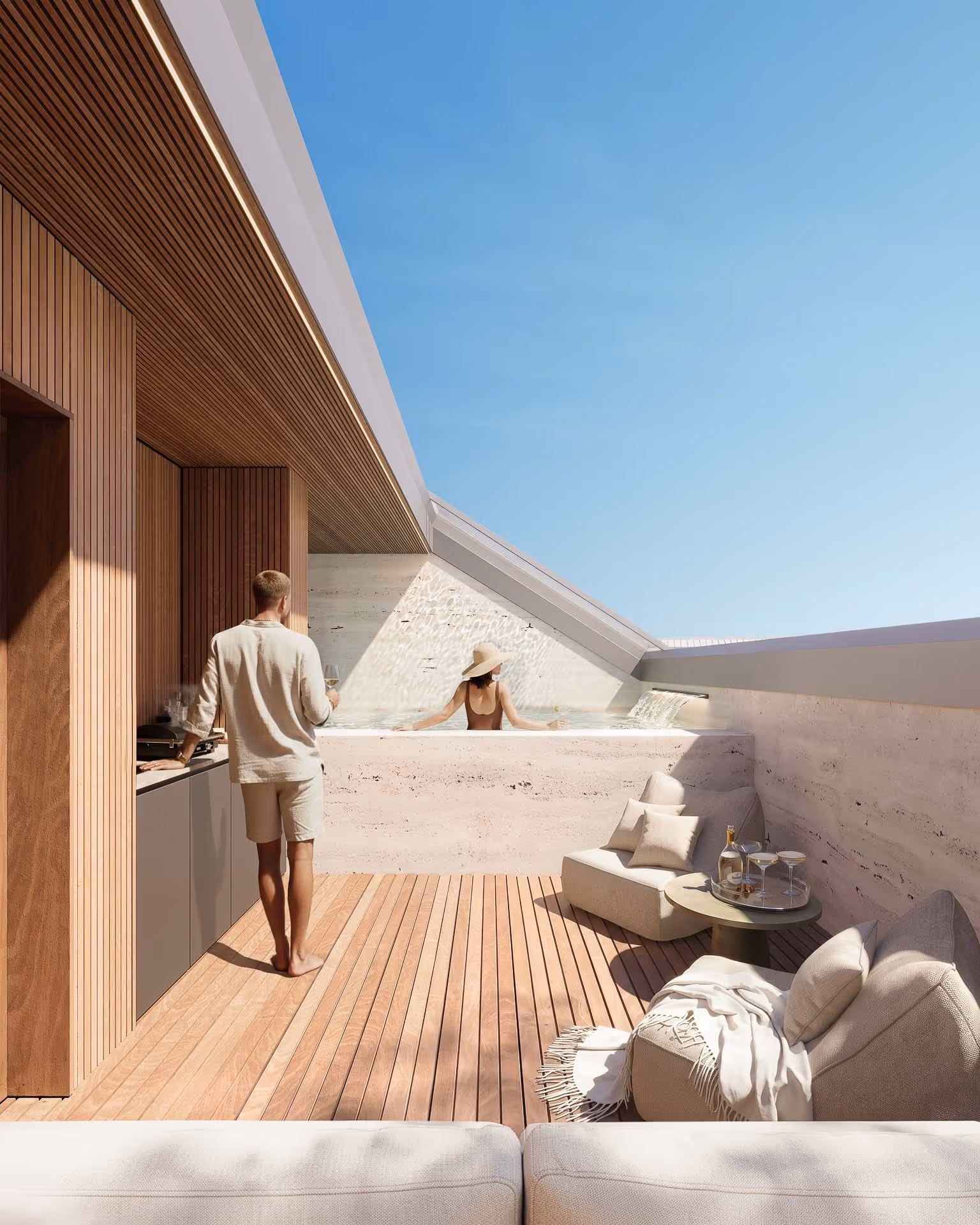 Espaço exterior com deck em madeira, duas cadeiras com almofadas, mesa com bebidas, homem com copo e mulher relaxando numa piscina sob um céu azul.
