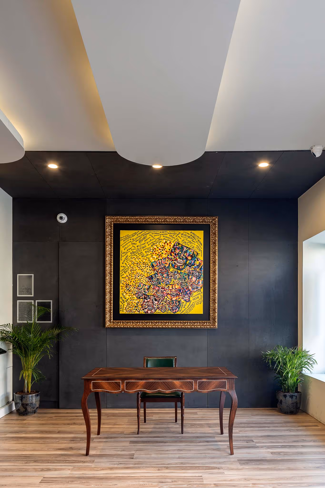 Mesa de madeira com cadeira verde em sala com parede preta e quadro abstrato amarelo.