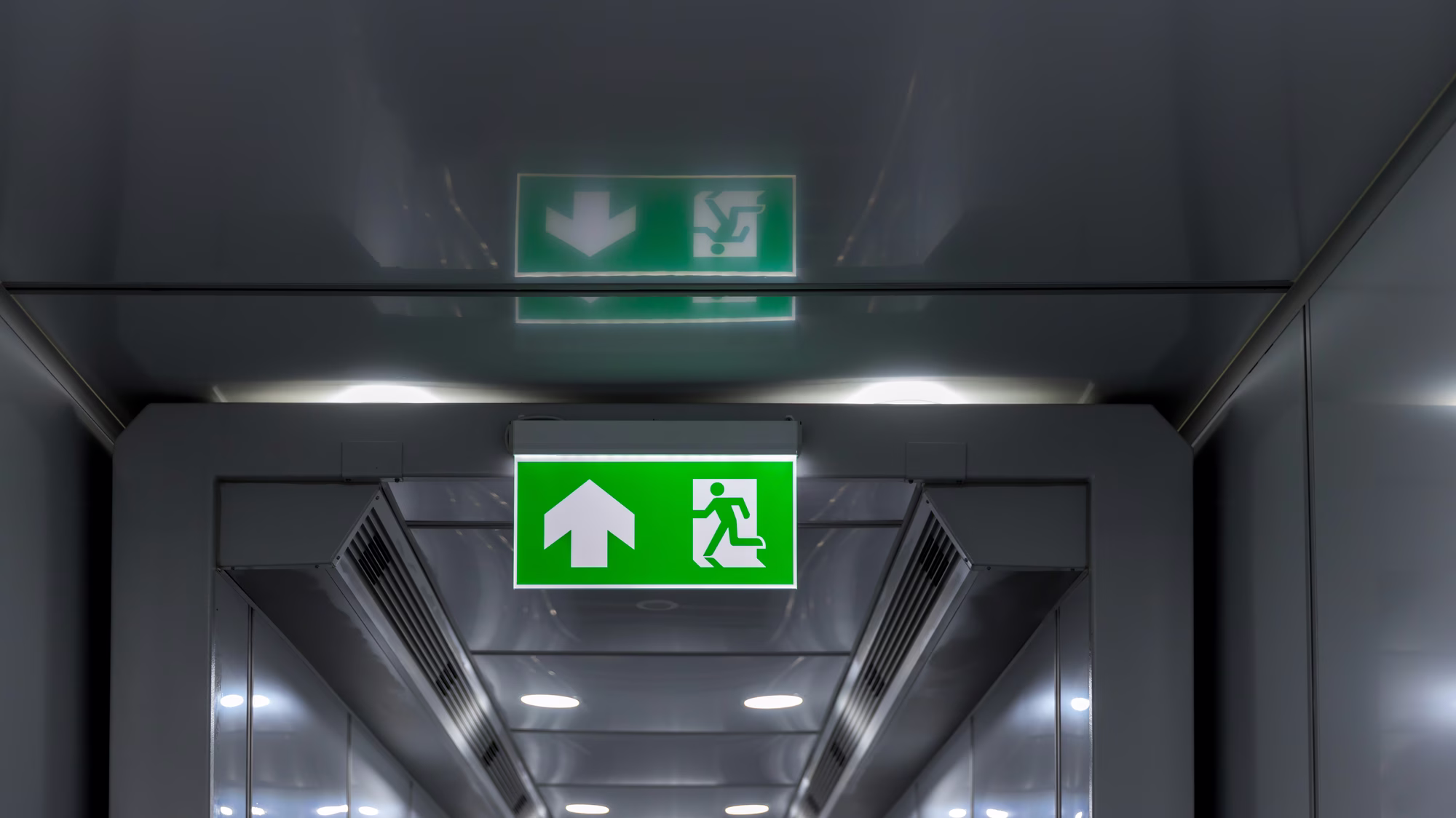 Illuminated exit signs in a grey corridor