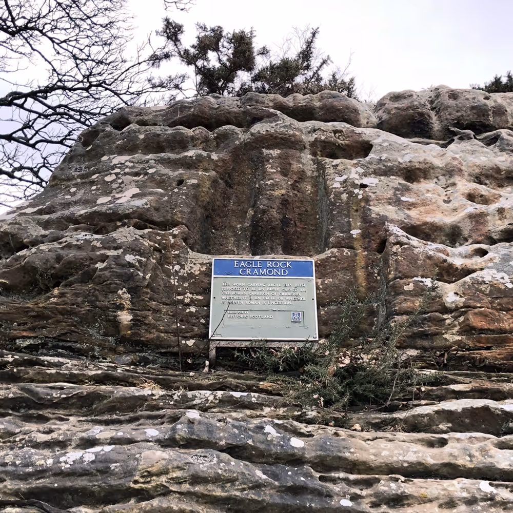 Rock formation with a weathered carving and a sign reading Eagle Rock Cramond by Historic Scotland.