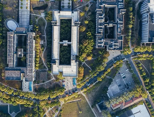 Top-down aerial view of a city block with modern buildings, tree-lined streets, and surrounding green spaces