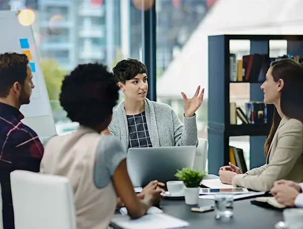 Team members in a meeting room discussing ideas around a table with a laptop and notes