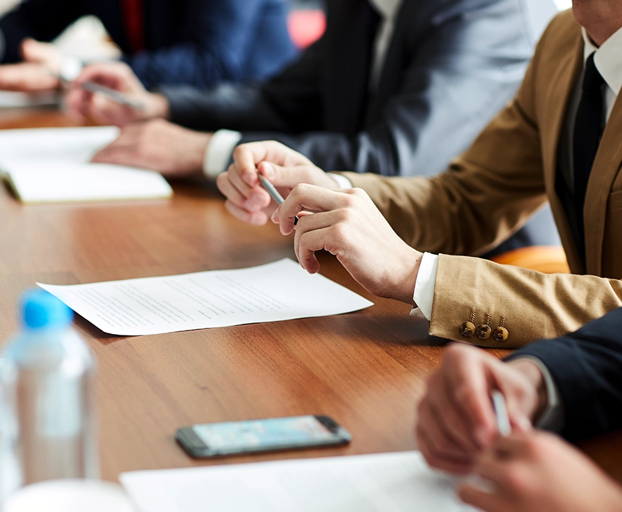 Business professionals seated at a meeting table with documents, pens, paper cups, and water bottles