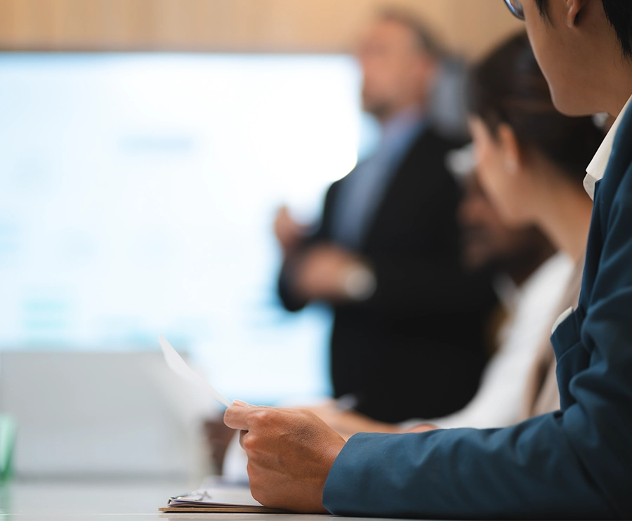 Team members in a meeting room listening to a presenter while reviewing printed documents