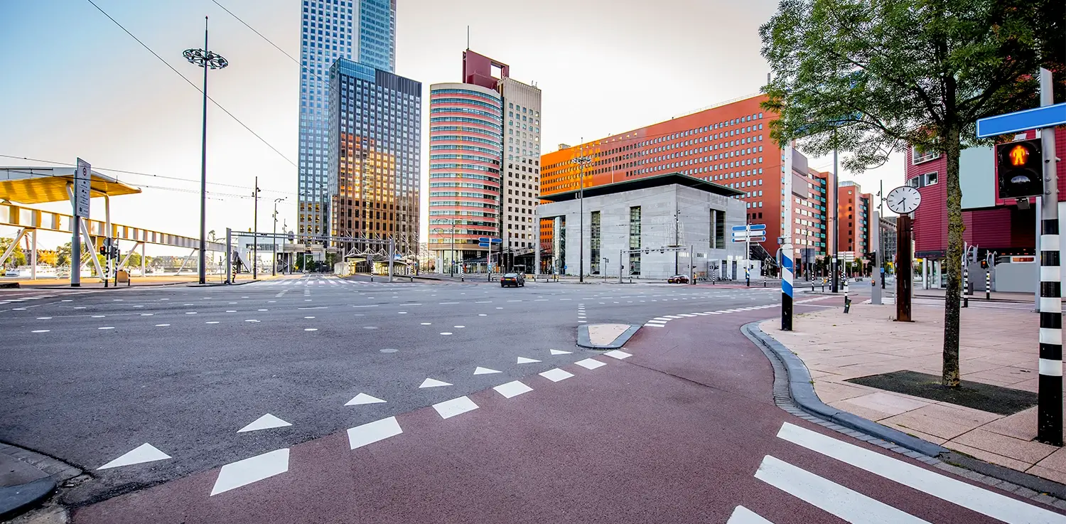 Wide urban intersection in Rotterdam with modern high-rise buildings, road markings, and pedestrian signals