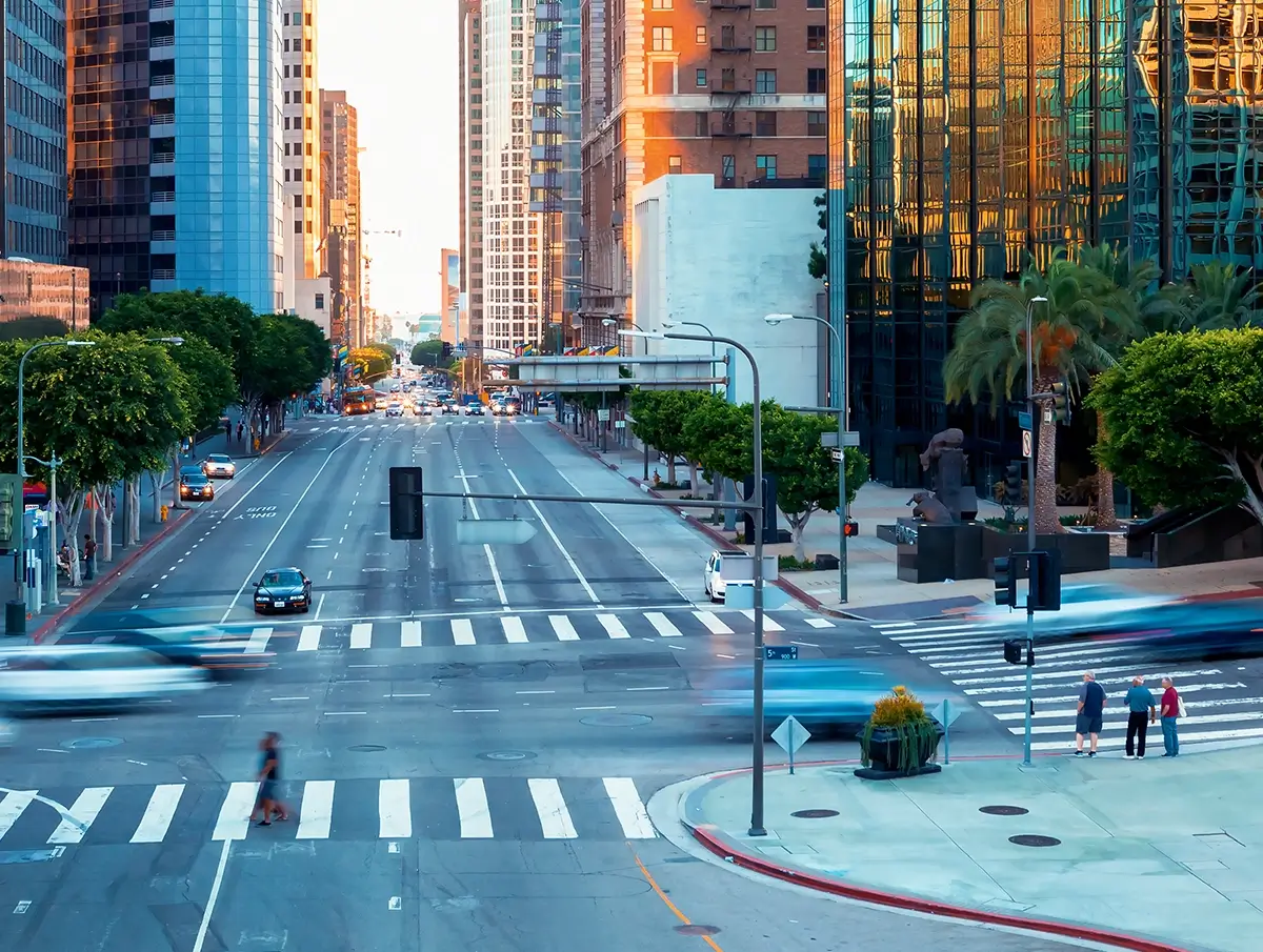 Wide view of a downtown Los Angeles intersection with office buildings, trees, crosswalks, and moving traffic