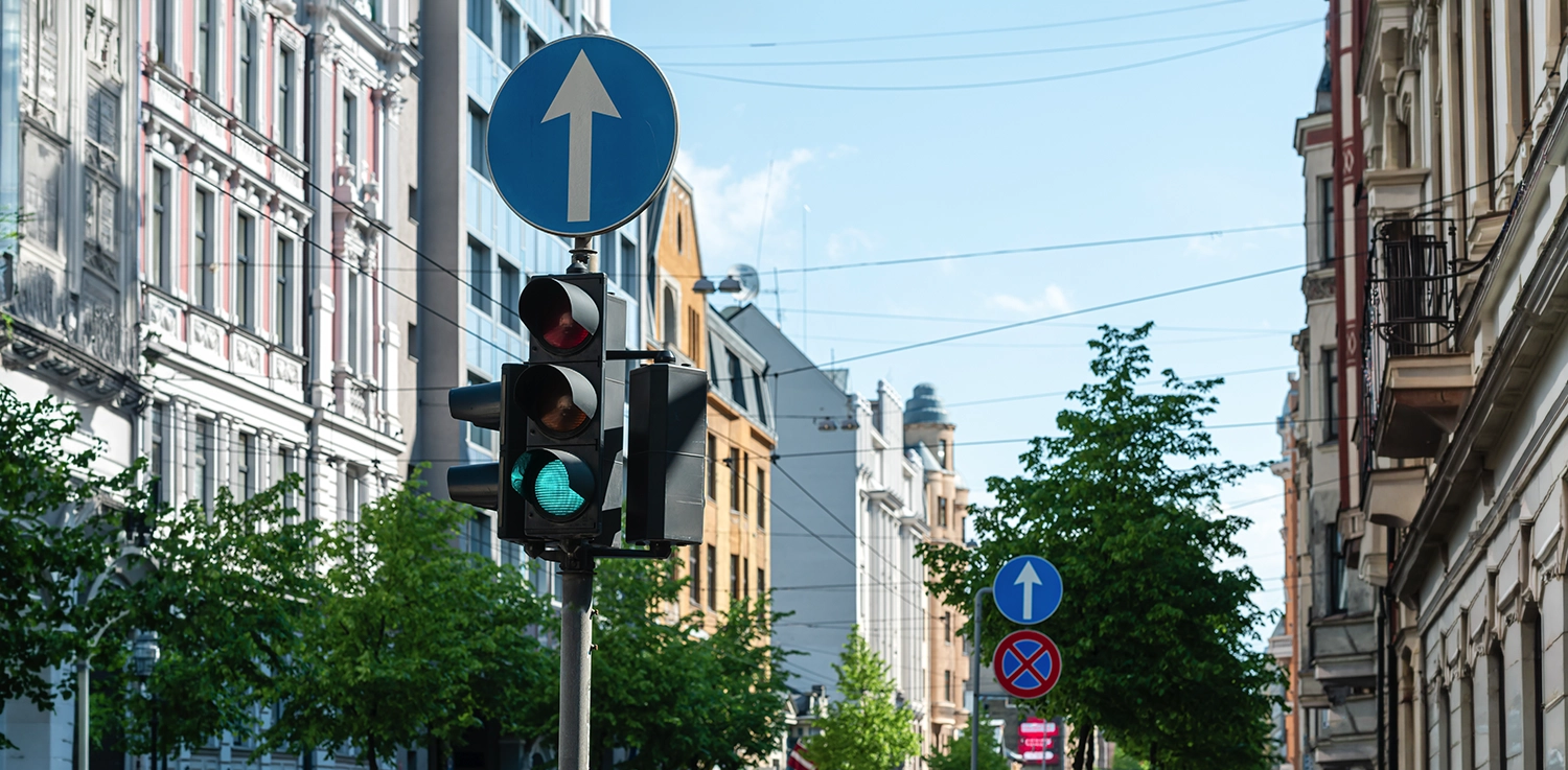 Traffic light with one-way street signs in a European city street lined with historic buildings and trees