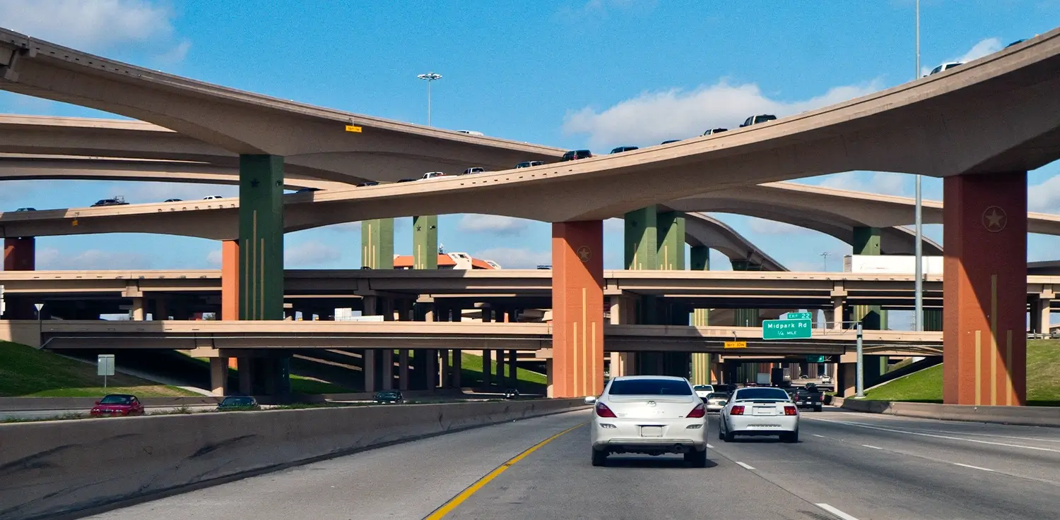 Cars driving on a freeway beneath a large multi-level highway interchange with curved overpasses