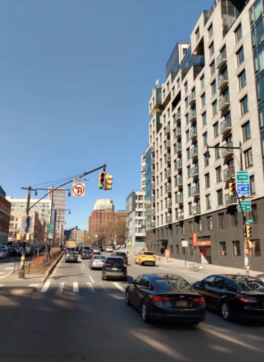 Wide city street with traffic, modern mid-rise buildings, and an urban intersection under a clear blue sky