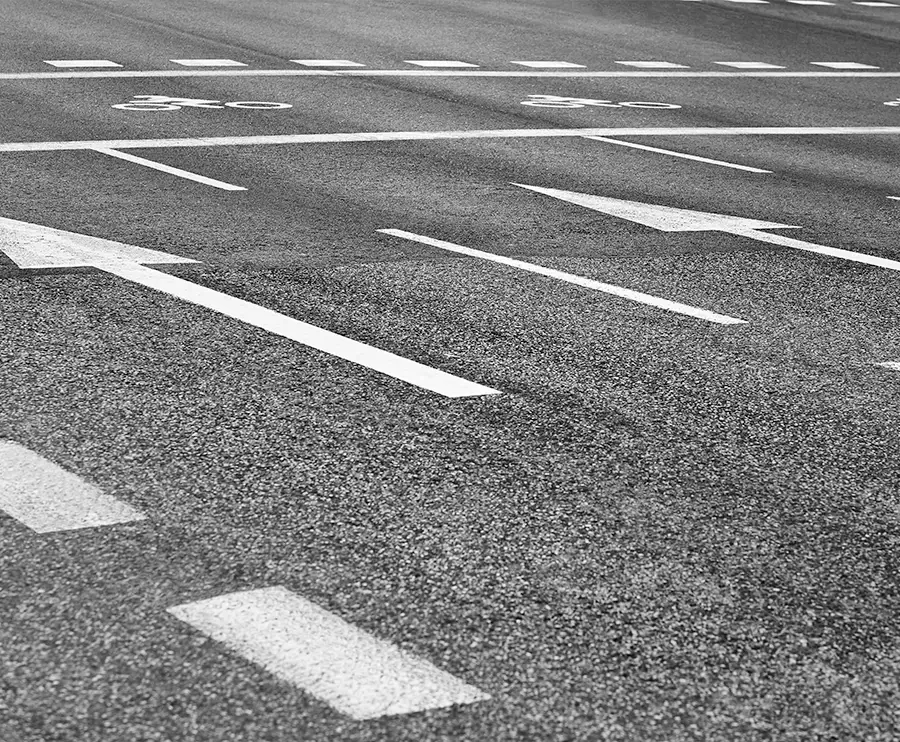 Close-up of asphalt road surface with white lane markings, directional arrows, and bike lane symbols