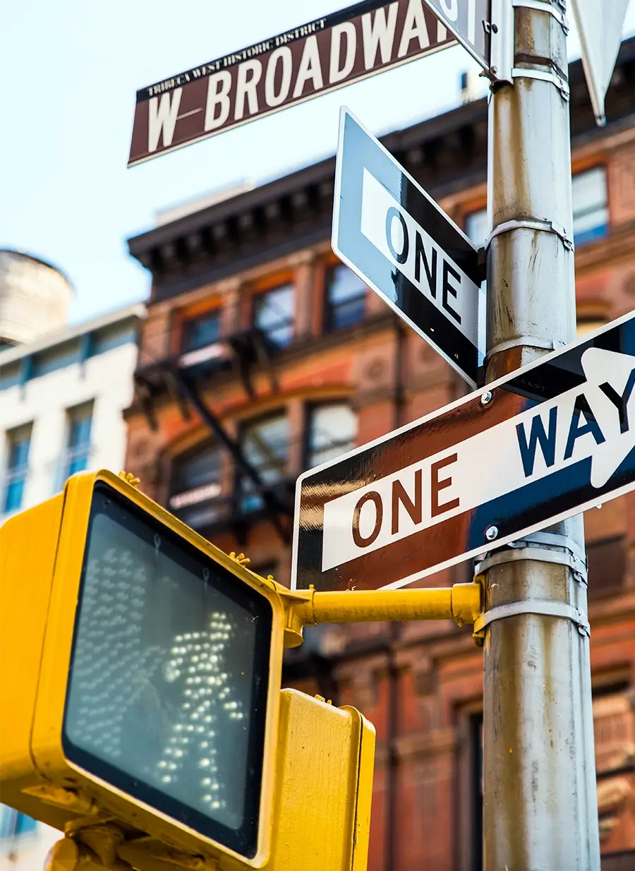 Broadway street sign with one-way traffic signs and a pedestrian crossing signal in an urban streetscape
