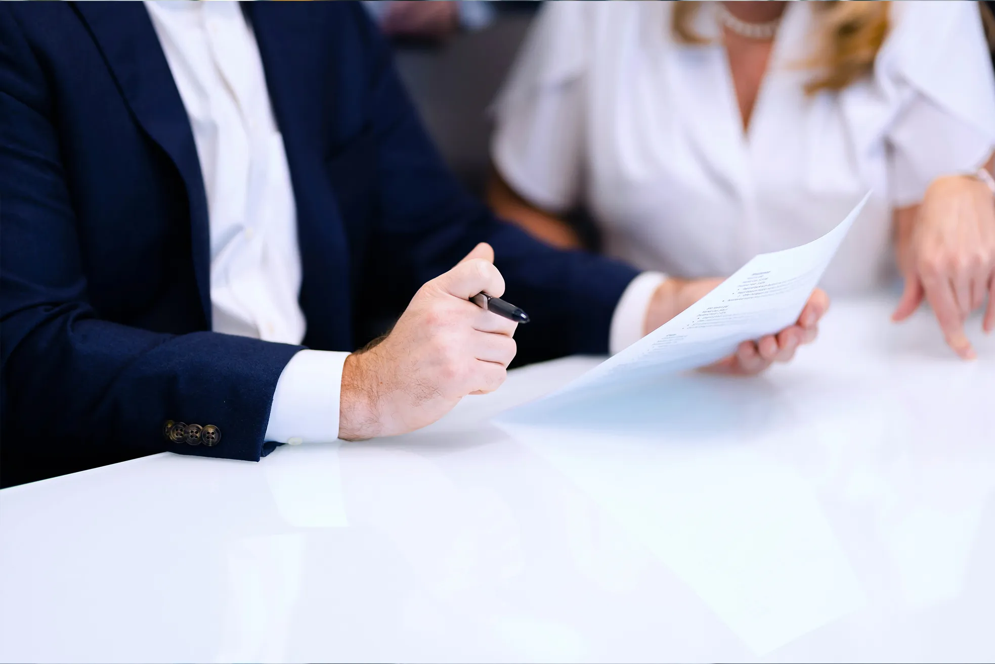 Two people reviewing a document together at a white table, one holding a pen and paper.