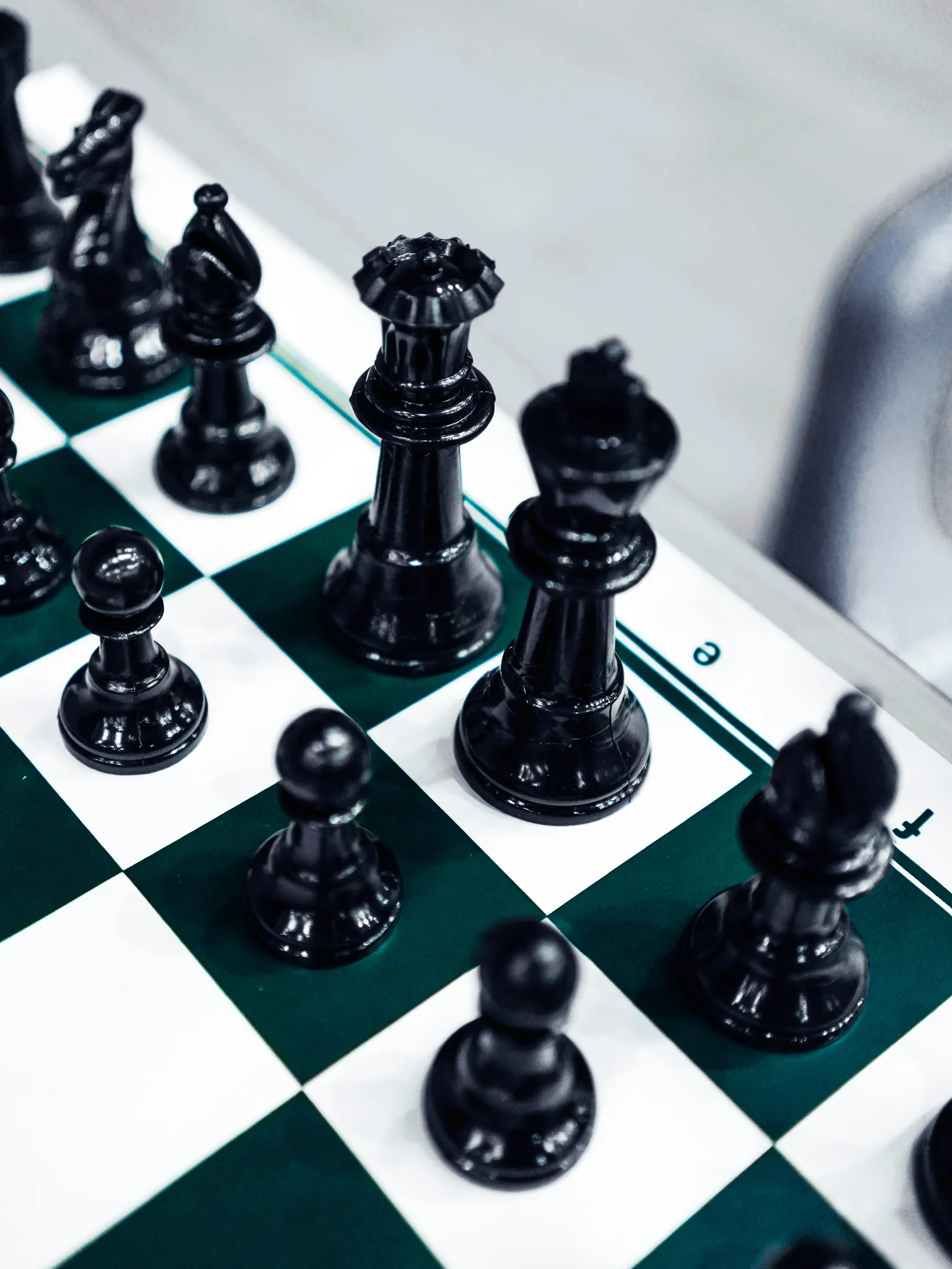 Close-up of black chess pieces including king, queen, bishop, knight, and pawns on a green and white chessboard.