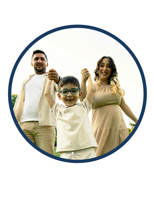 Smiling parents lifting their young son by his hands outdoors on a bright day.