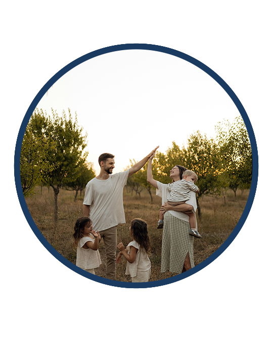 Man and woman high-fiving outdoors with three children around them at sunset in an orchard.