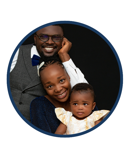 Smiling man, woman, and baby posed closely together on a black background.