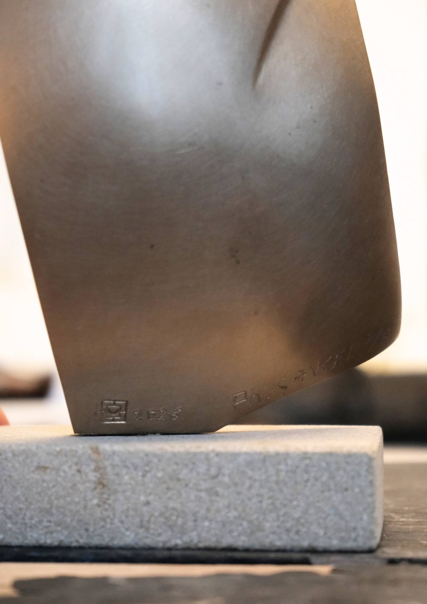 Détail de la base de la sculpture Affection de l'Atelier Philippe Gancel en bronze poli sur socle en pierre et de la signature gravée Ph. GANCEL sur une sculpture en métal.