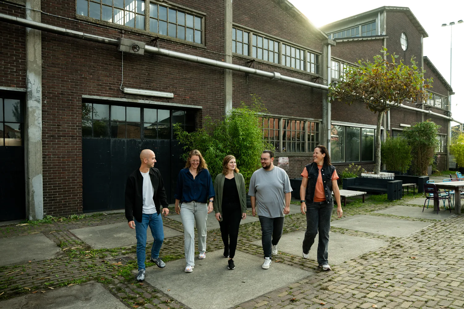 Het team van Buro Staal loopt over het plein tussen de fabriekshallen.