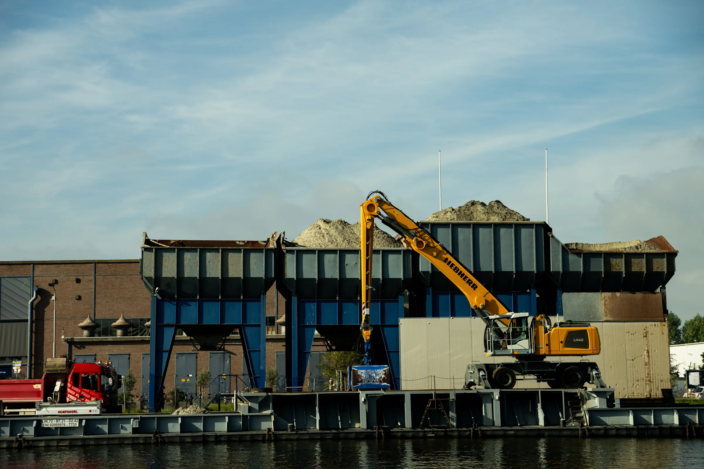 Industrieel terrein aan het water met een gele kraan en bulkopslag.
