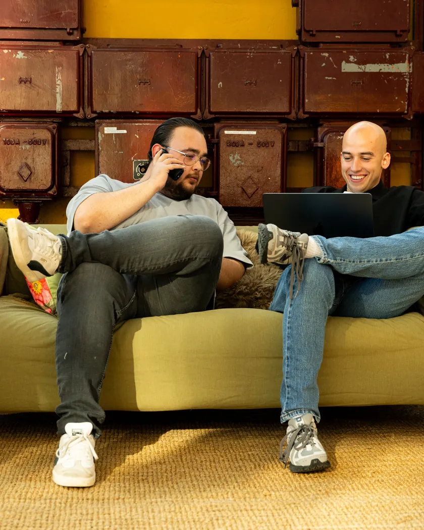 Coen en Kevin van Buro Staal op de bank, de een belt, de ander werkt op een laptop
