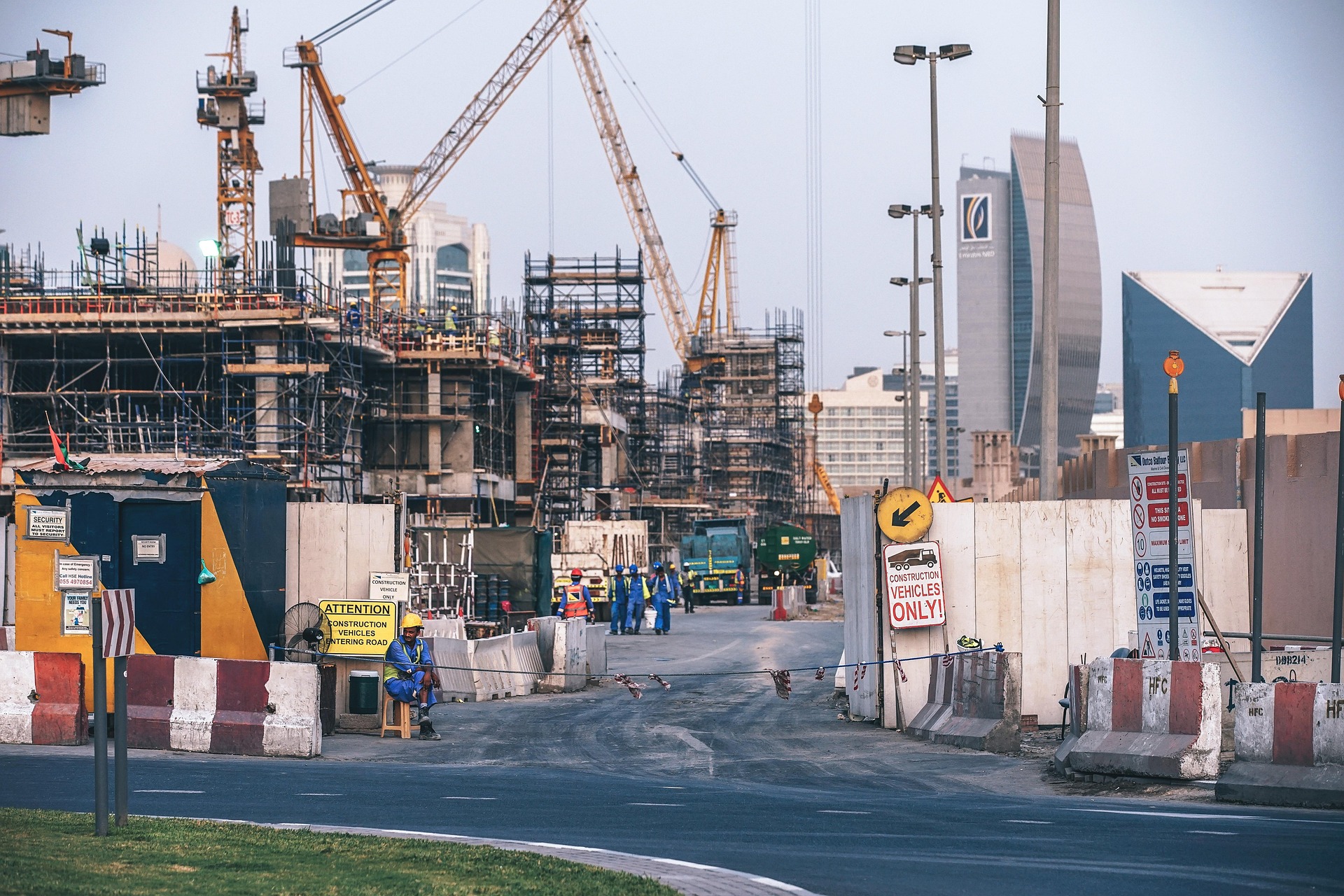 Cranes and scaffolding on an active construction site in Dubai, with the Emirates NBD tower on the skyline behind