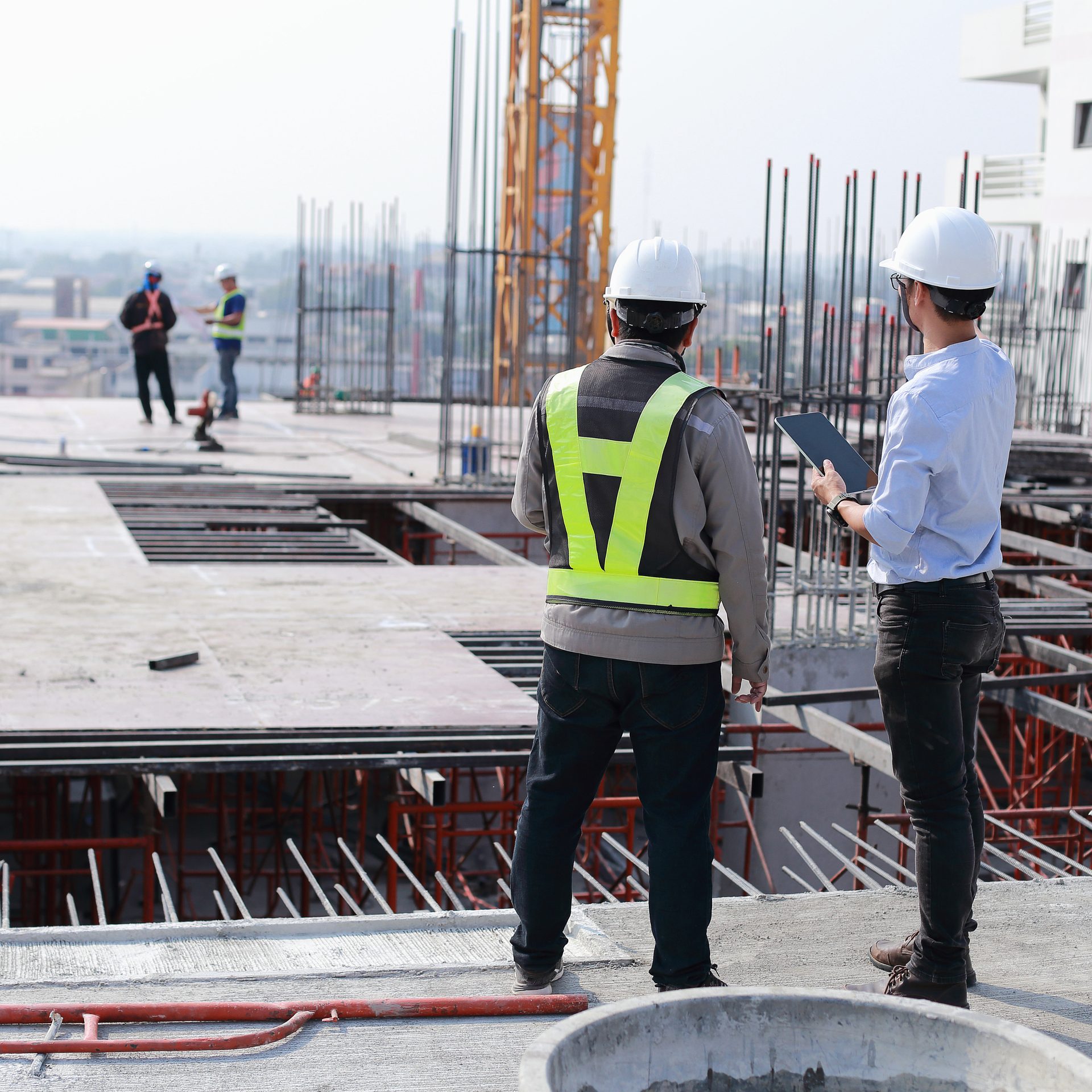 Two site supervisors in hard hats reviewing a tablet on the upper floor of a building nearing completion