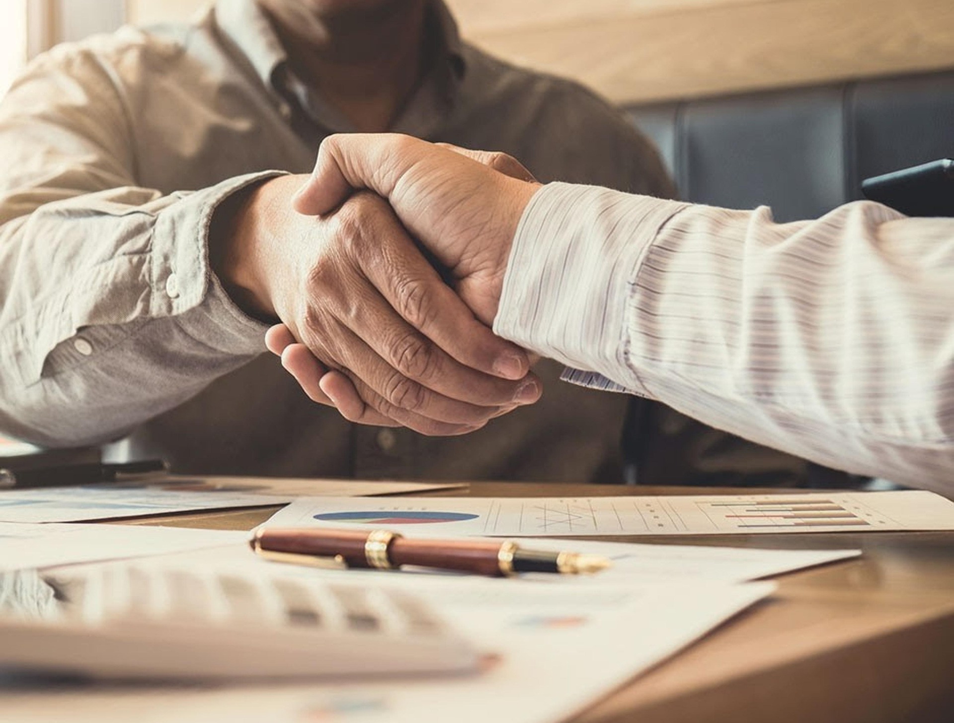 Two people shaking hands across a desk covered with documents and a pen, marking the completion of a property handover