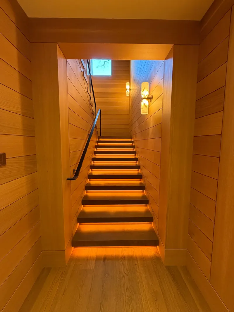 Indoor wooden staircase with warm under-step lighting and modern wall sconces.