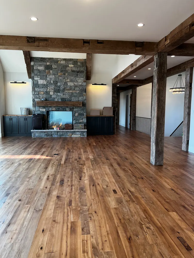 Spacious room with wooden floor, exposed wooden beams, stone fireplace, and built-in cabinets.