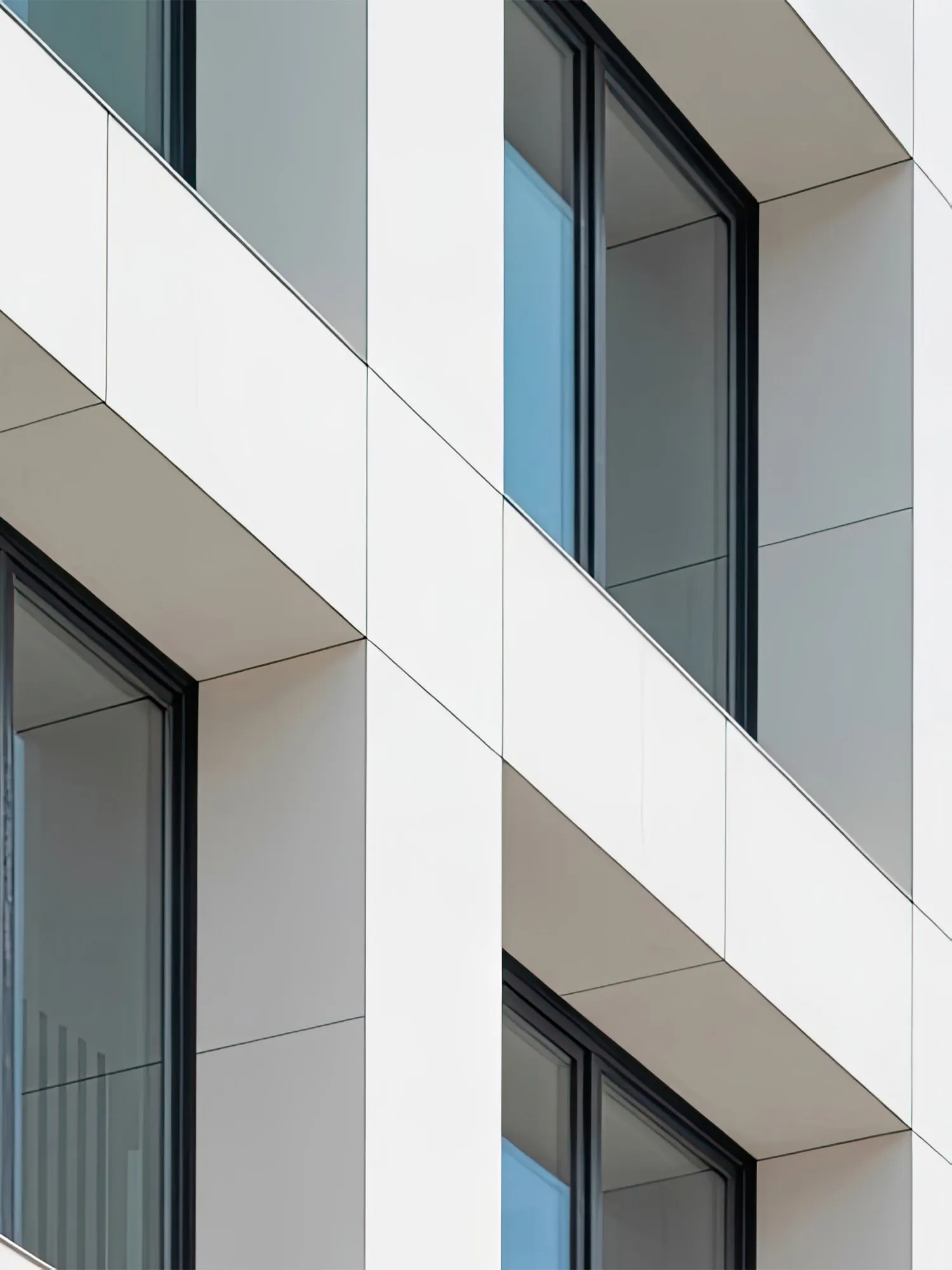 Moderne weiße Fassade mit schwarzen Fensterrahmen und Glasflächen in einem Gebäude.