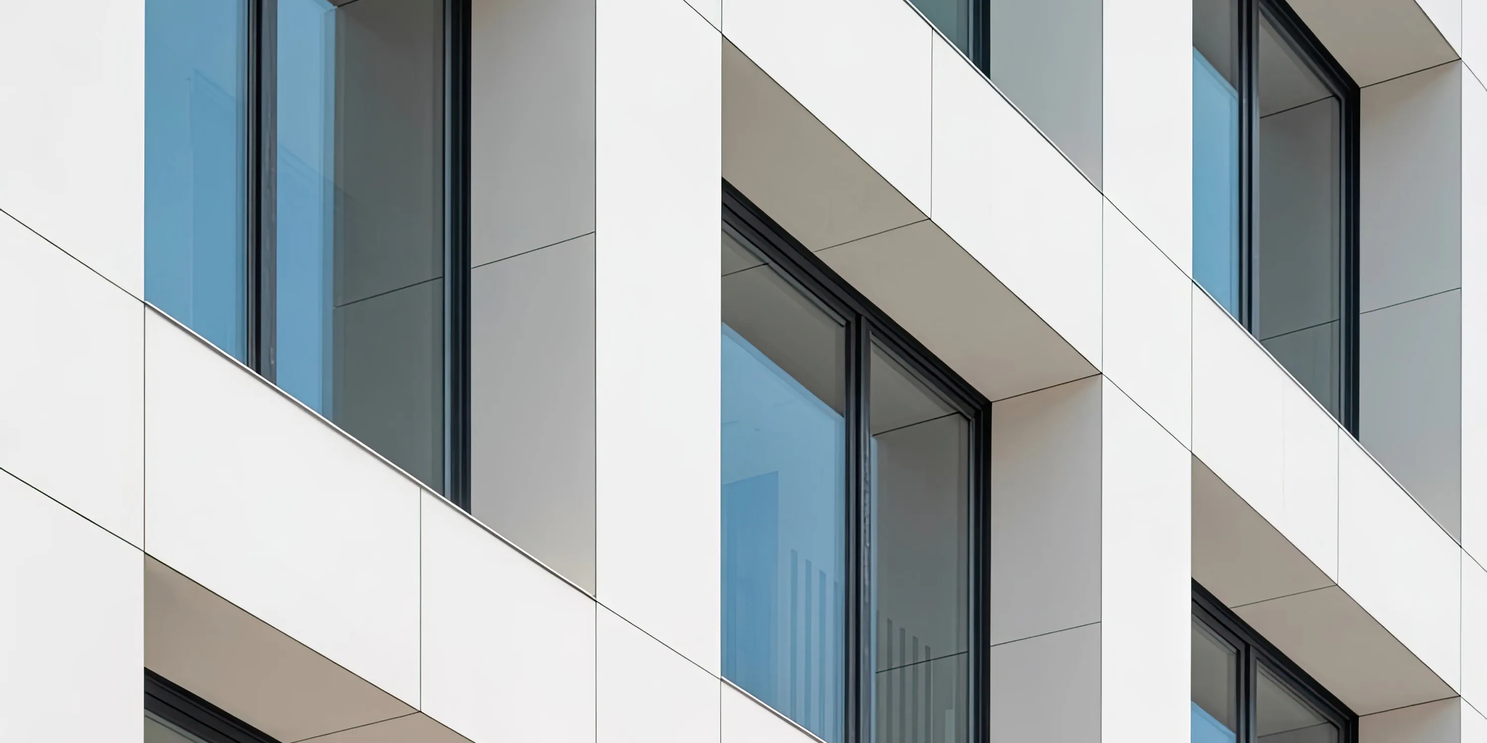 Moderne Fassade mit weißen Platten und großen Fenstern mit schwarzem Rahmen.