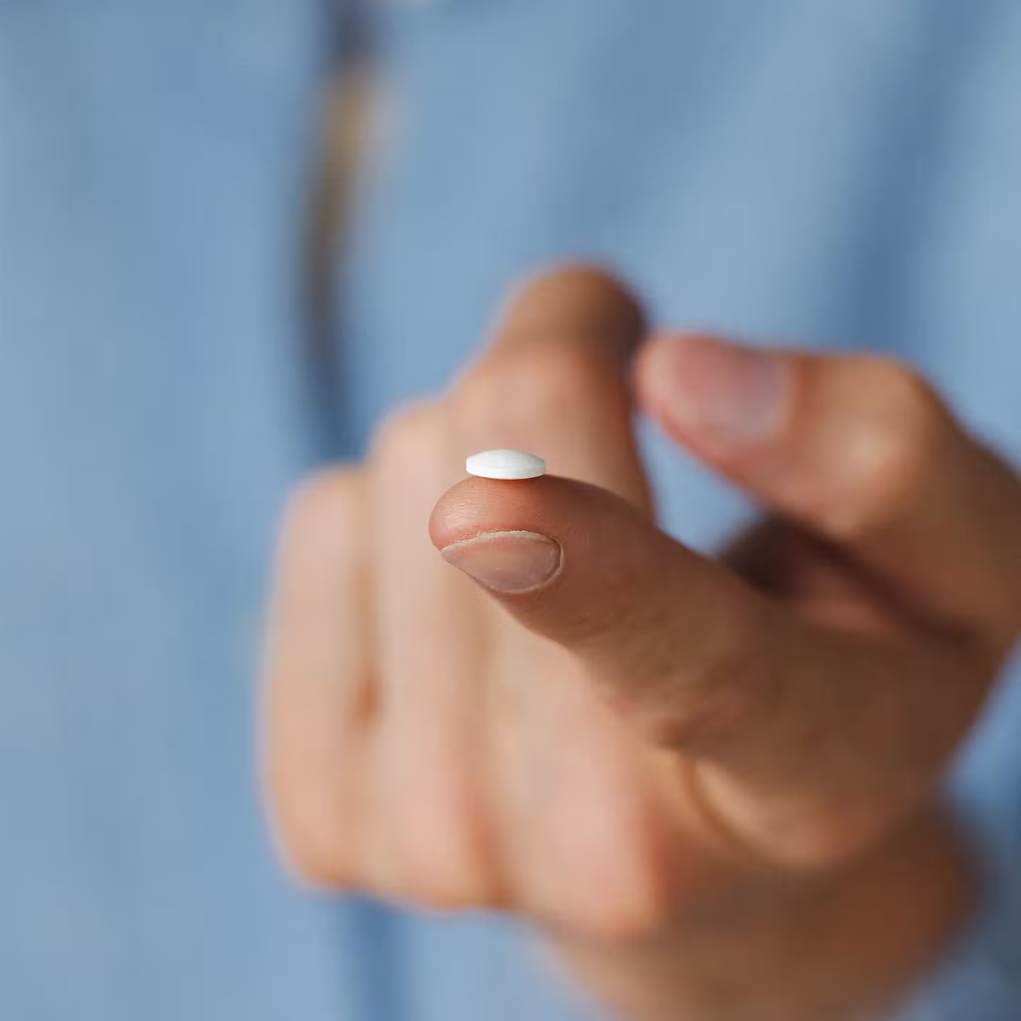 En hand håller en liten vit tablett mot ett finger mot en blå bakgrund