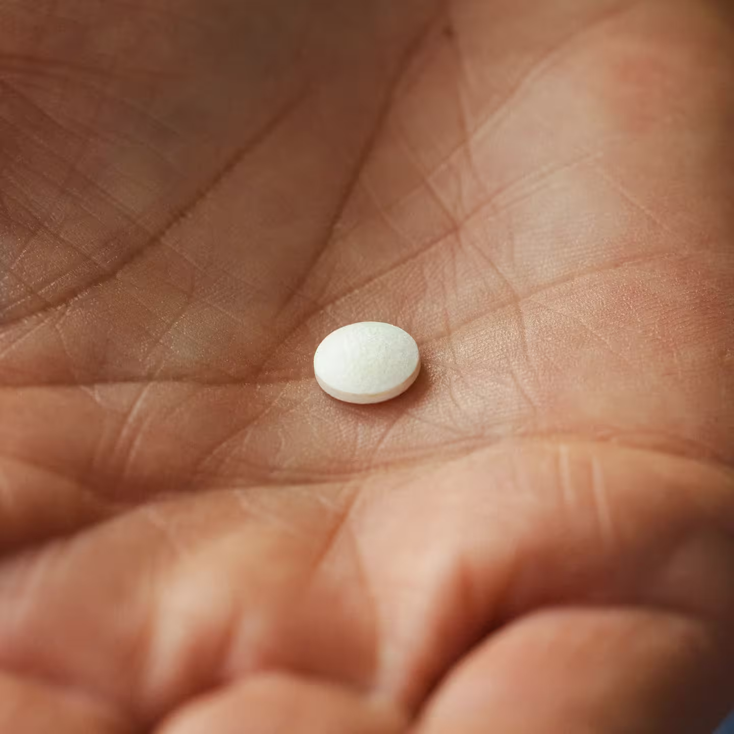 En liten vit tablett ligger i en öppen handflata