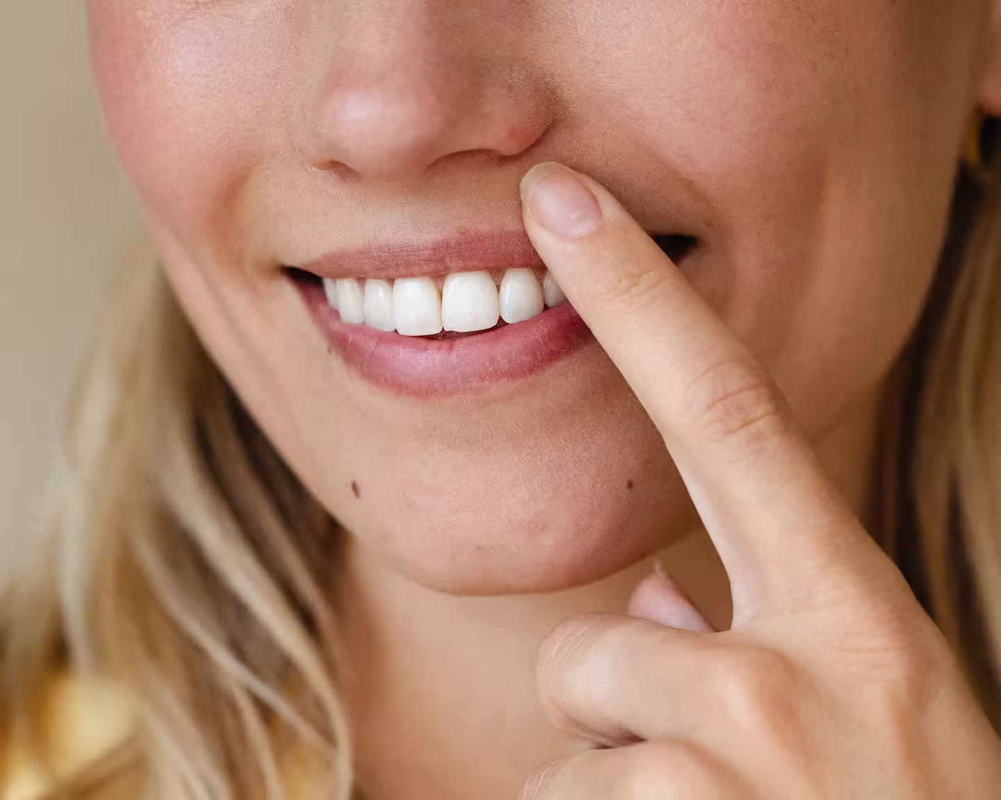 Närbild på en blond kvinnas mun med ett finger mot läppen och vita tänder synliga