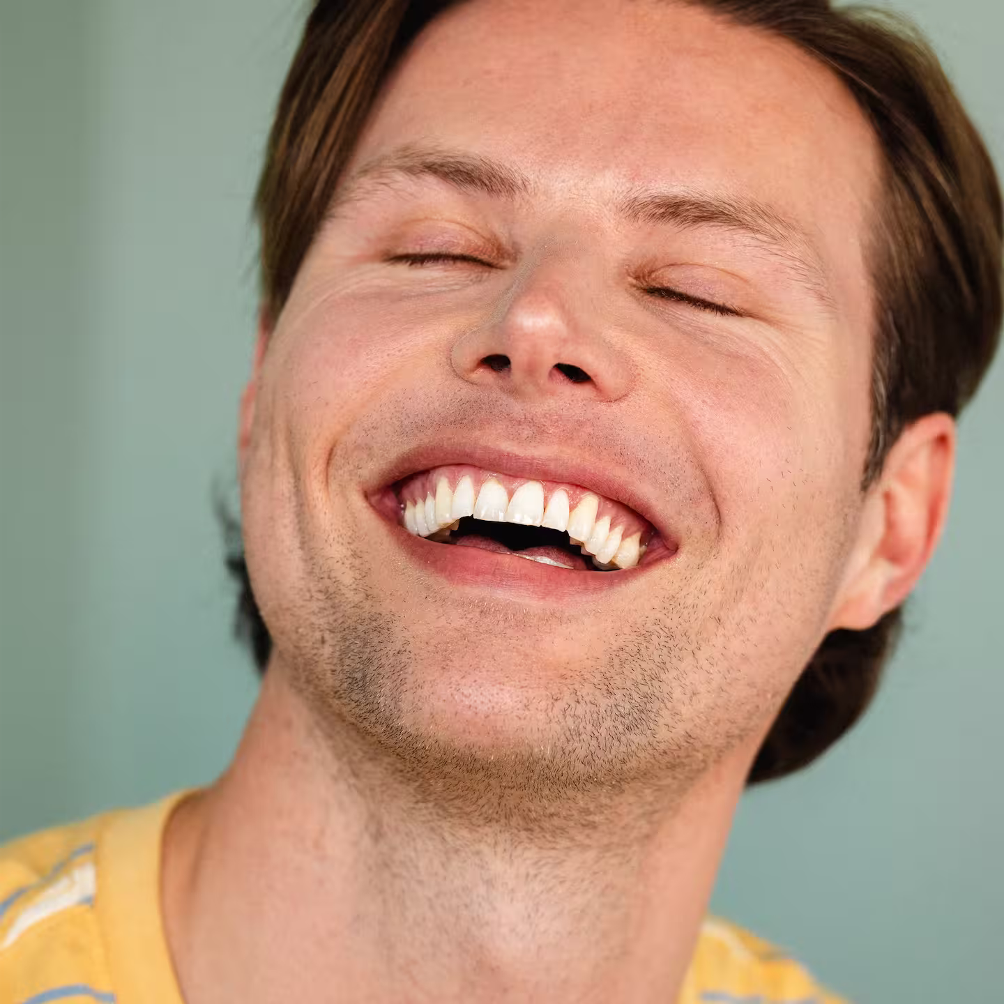En ung man i gul t-shirt skrattar med stängda ögon