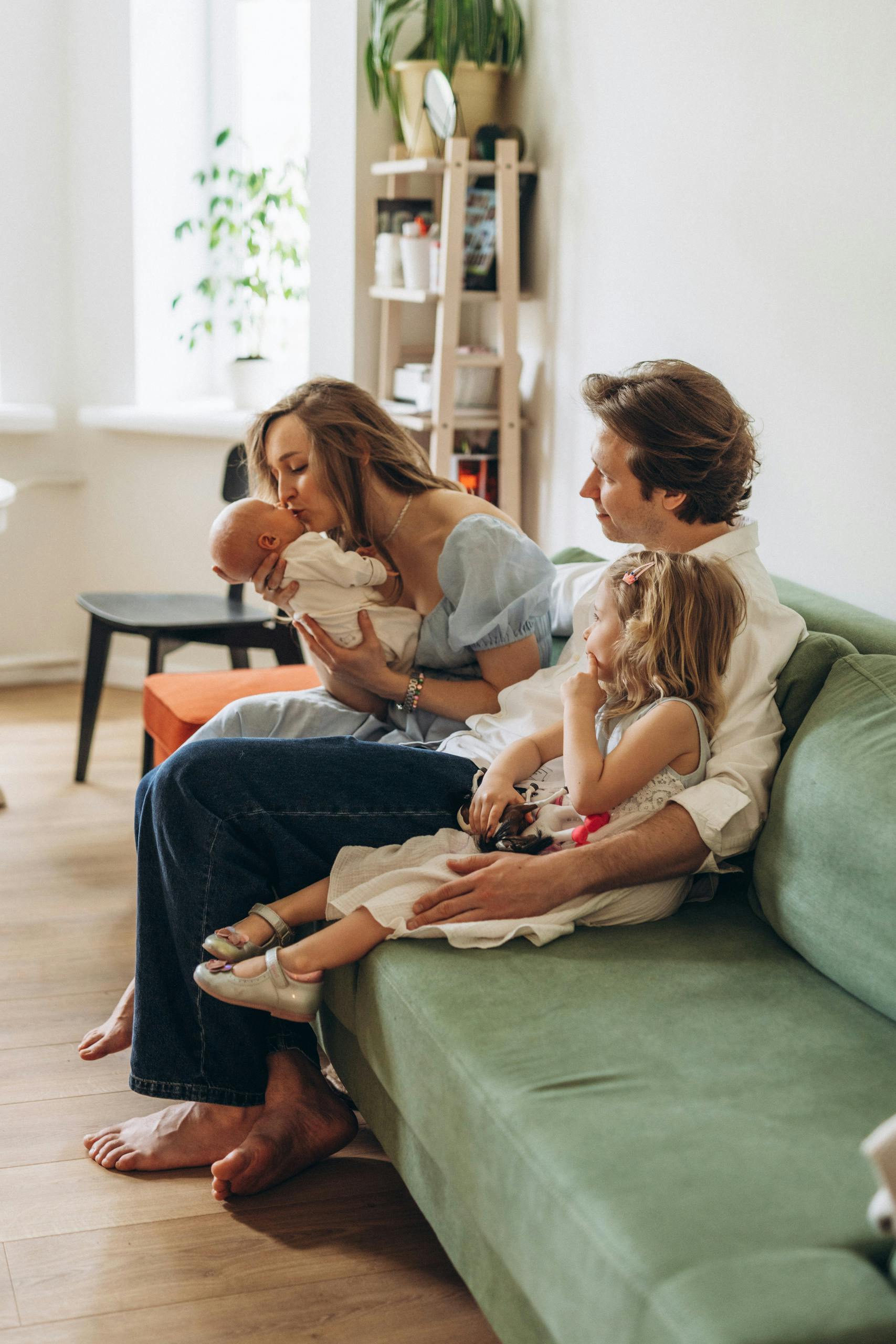 Family sitting on green sofa with infant stock image