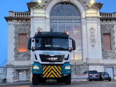 Camion de chantier garé devant un grand bâtiment ancien en pierre au crépuscule.