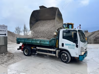 Camion benne en train de décharger du gravier dans un chantier de construction par temps nuageux.