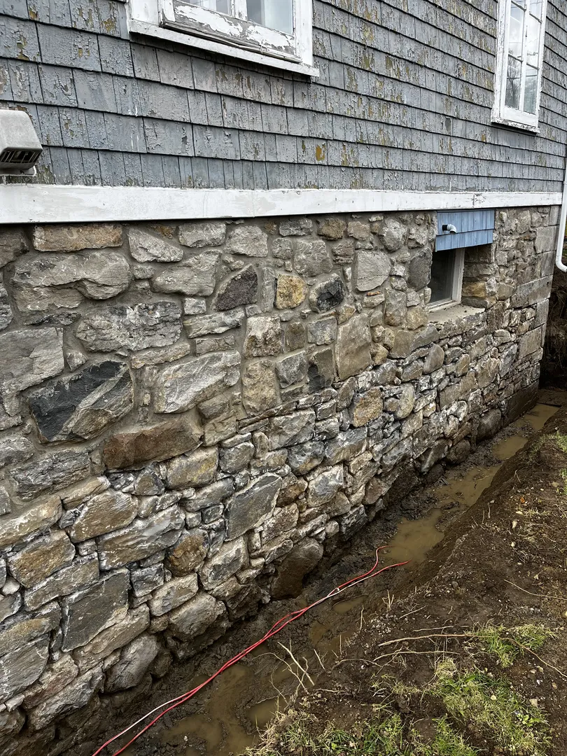 Mur de fondation en pierre avec des pierres de différentes tailles et couleurs assemblées au mortier.