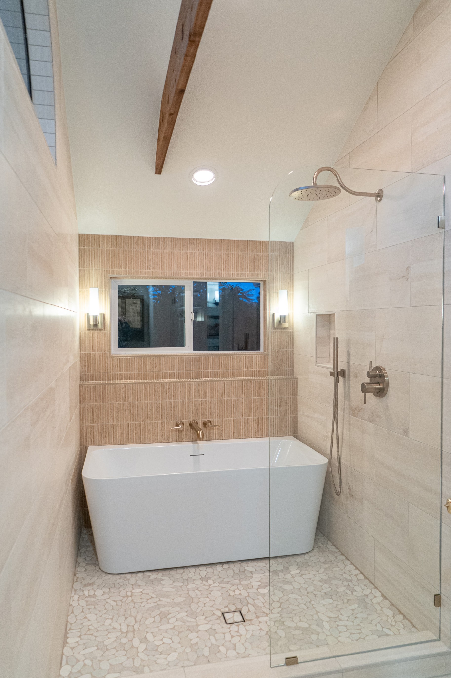 Modern bathroom shower with glass doors, marble walls, mosaic tile floor, and black rain showerhead and fixtures.