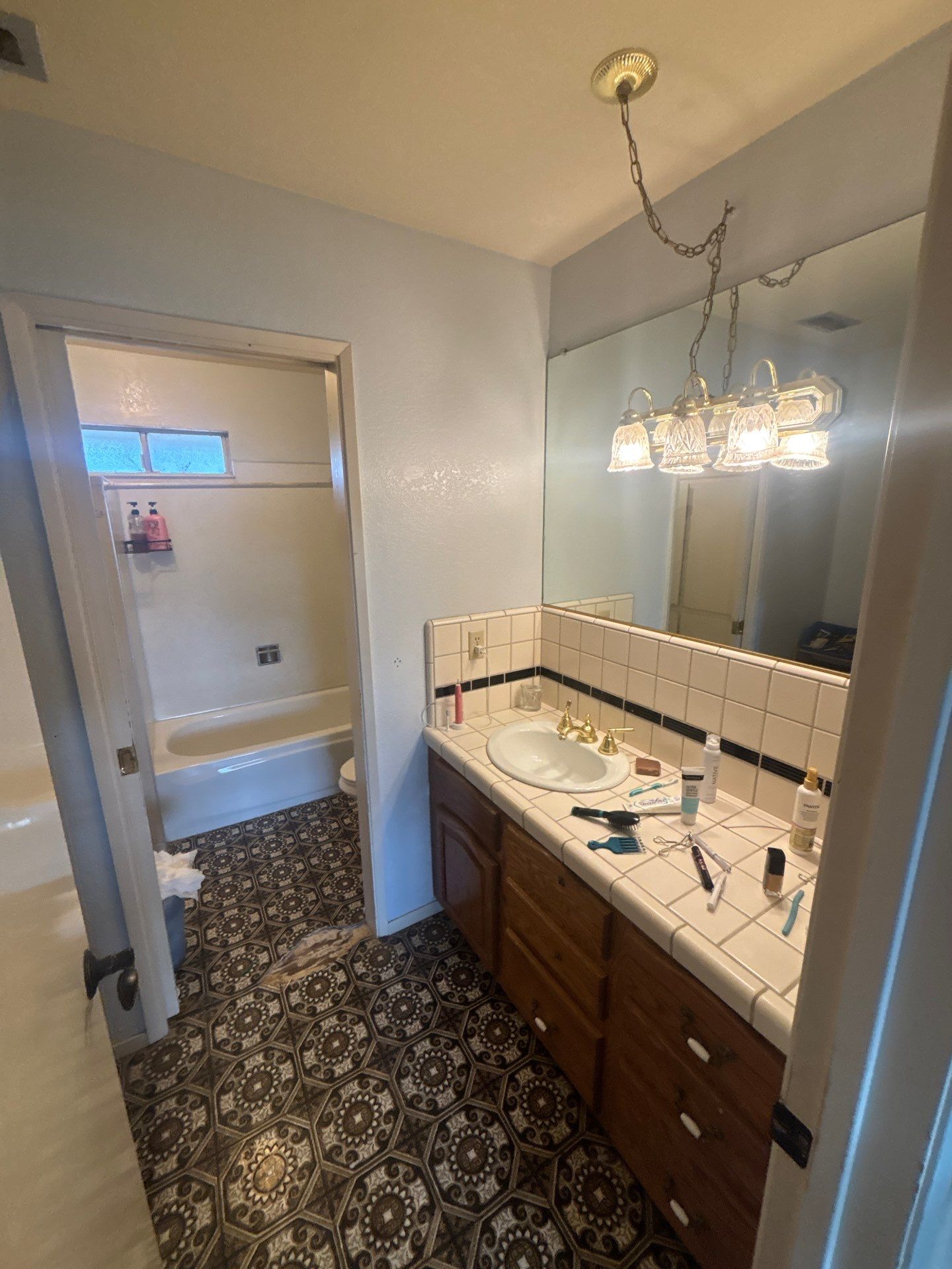 Modern Sacramento bathroom with a large bathtub, double sink vanity with cluttered countertop, tile flooring, and glass shower enclosure.
