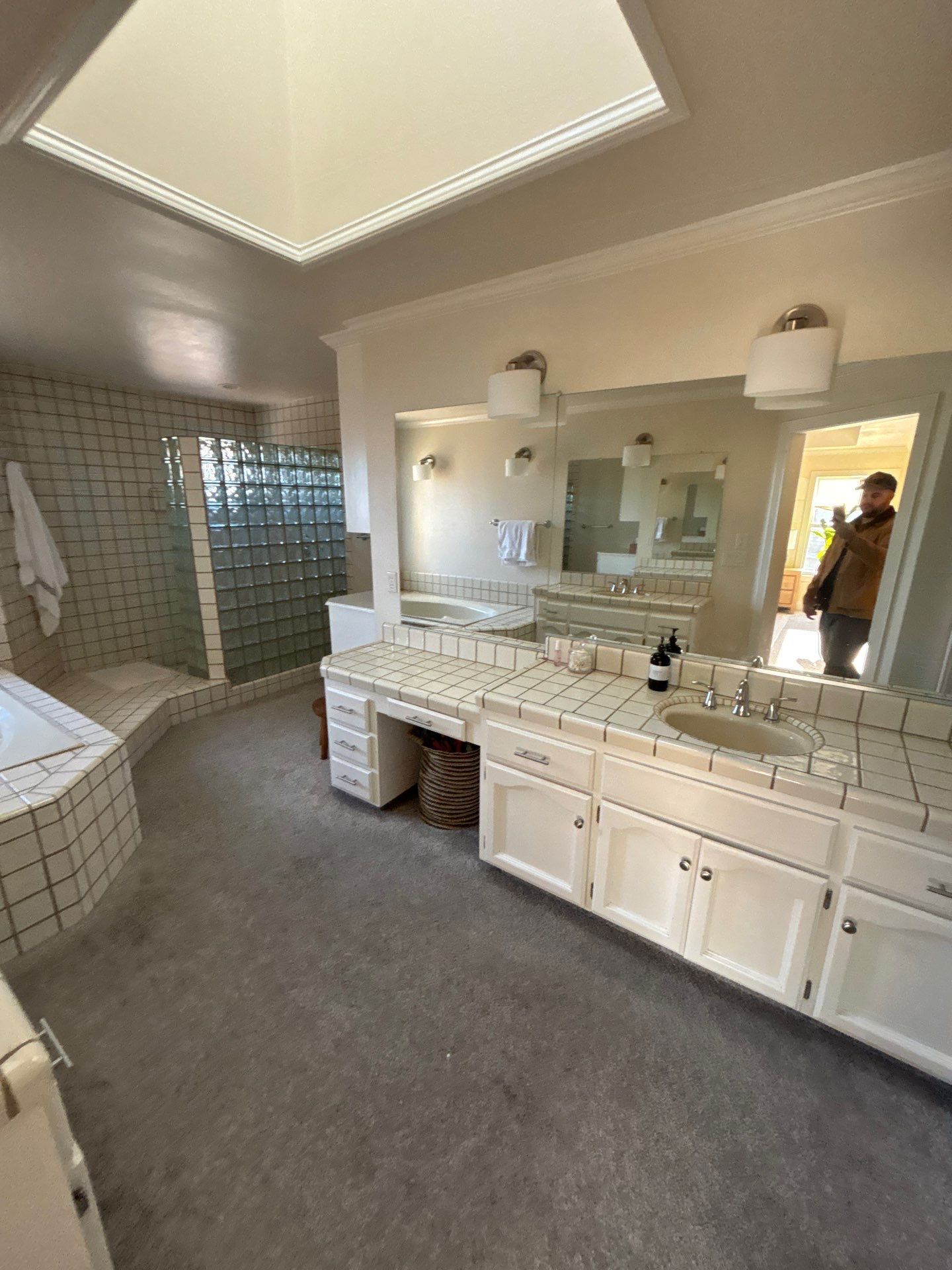 Modern Sacramento bathroom with a large bathtub, double sink vanity with cluttered countertop, tile flooring, and glass shower enclosure.