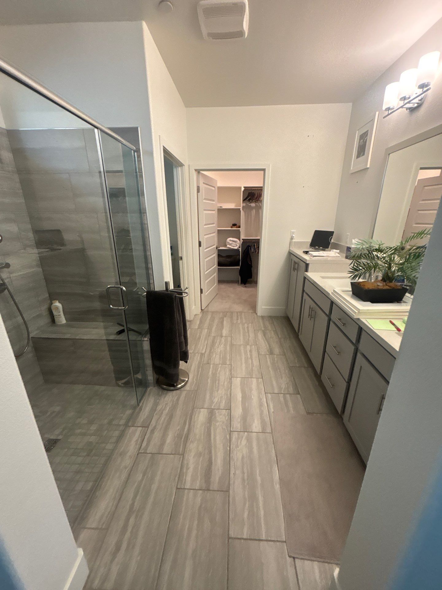 Modern Sacramento bathroom with a large bathtub, double sink vanity with cluttered countertop, tile flooring, and glass shower enclosure.
