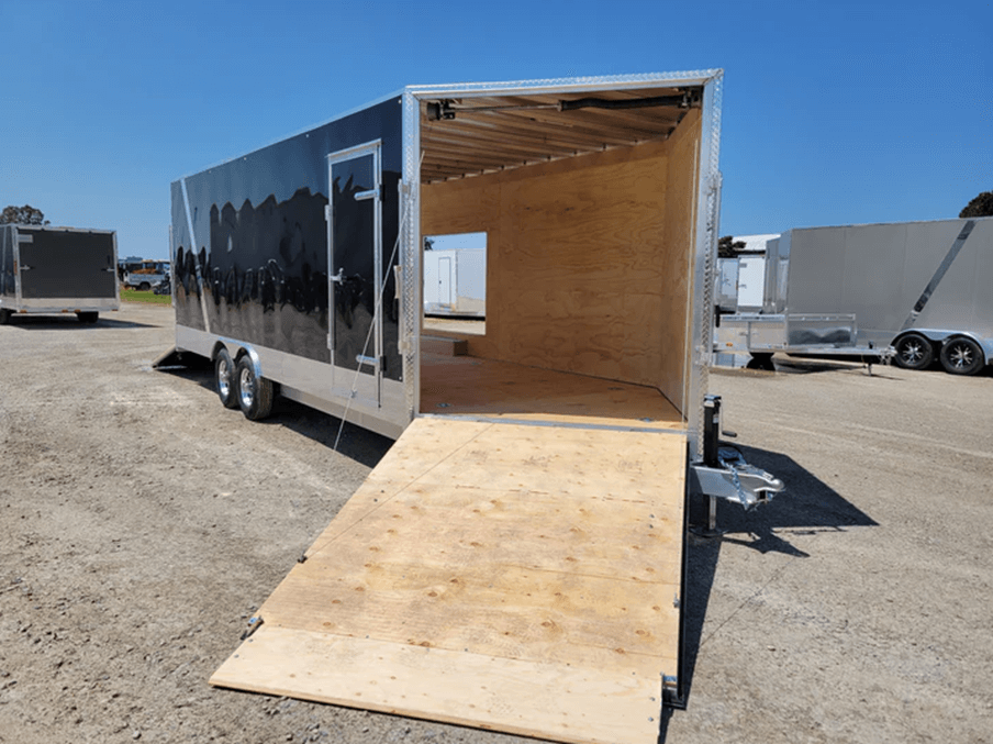 Black enclosed trailer with open rear door ramp showing an empty wooden interior under clear sky.