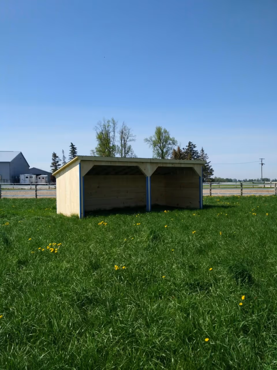 Wooden two-compartment shelter in a green grassy field with a clear blue sky.