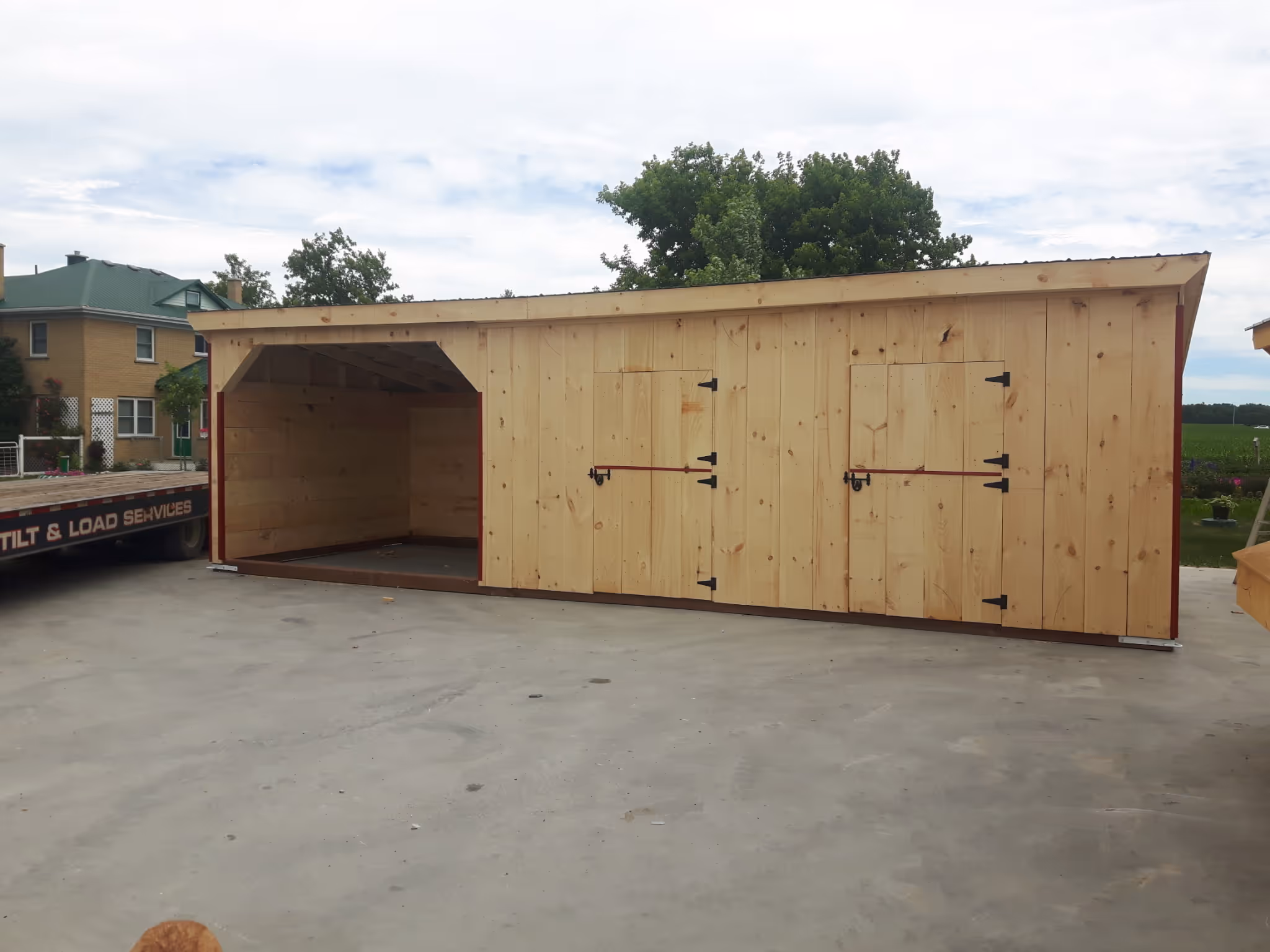 Large wooden shed with two closed doors and an open storage area on a concrete surface.
