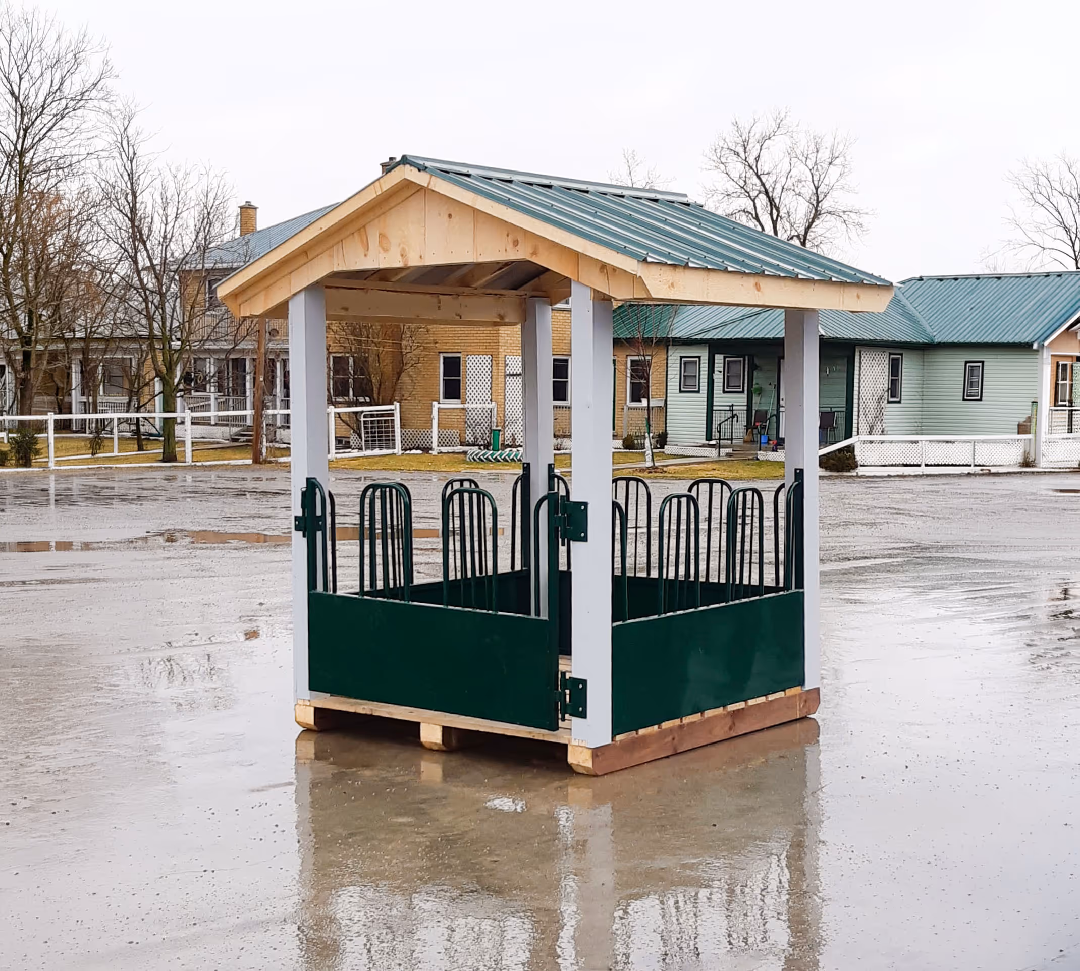 Small wooden shelter with green rails and a metal roof on wet concrete outdoors.