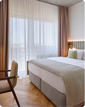 Moderní hotelový pokoj s velkou postelí, židlí a závěsy na okně s výhledem ven.