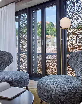 Modern room with patterned glass doors, grey chairs, ottoman, round table, and a floor lamp.