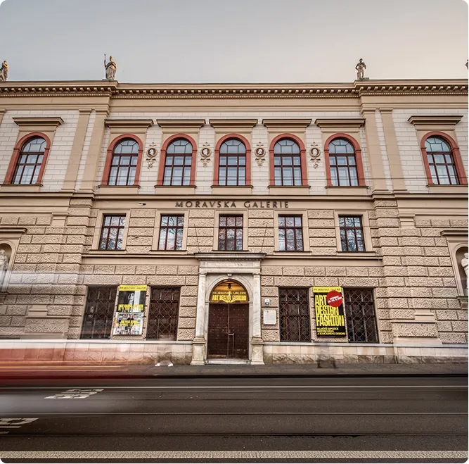 Budova Moravské galerie s vchodem a žlutými plakáty na výstavu umění, designu a módy.